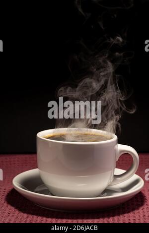 Coffee steaming in a cup with saucer isolated on a black background on a red surface Stock Photo
