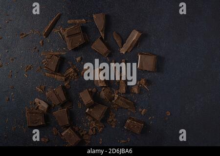 Dark chocolate broken into pieces isolated on a dark background. Top view, flat lay. Free space for text. Stock Photo