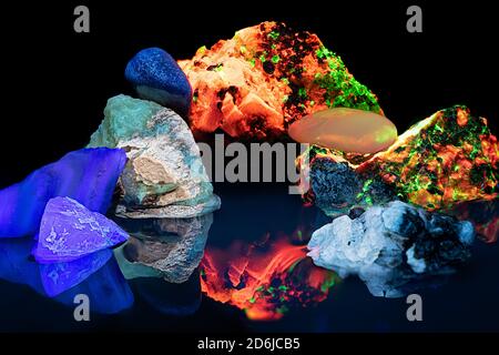 Fluorescent minerals under ultraviolet light sit in a small pool of water with reflections Stock Photo