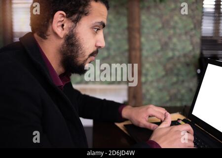 Young black male  developer sitting in pizza restaurant, drinking coffee or  tea and working with laptop. Stock Photo