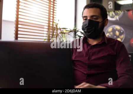 African businessman or developer wearing surgical face mask in the restaurant and typing on laptop - concept on new normal everyday lifestyle and peop Stock Photo
