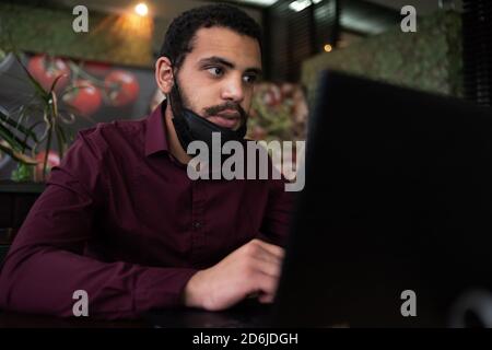 African businessman or developer wearing surgical face mask in the restaurant and typing on laptop - concept on new normal everyday lifestyle and peop Stock Photo
