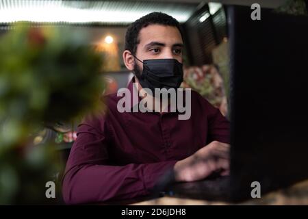 African businessman or developer wearing surgical face mask in the restaurant and typing on laptop - concept on new normal everyday lifestyle and peop Stock Photo