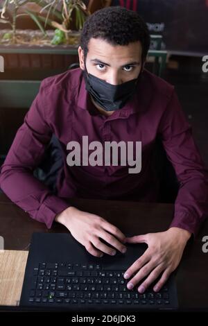 African businessman or developer wearing surgical face mask in the restaurant and typing on laptop - concept on new normal everyday lifestyle and peop Stock Photo