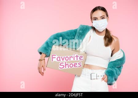 young woman in medical mask holding box with favorite shoes lettering on pink Stock Photo