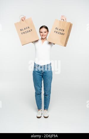 young joyful woman holding shopping bags with black friday lettering on white Stock Photo