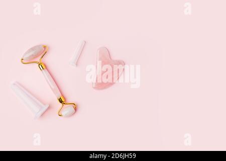 Pink Gua Sha Stone, roller facial massage tools. Rose Quartz jade roller and stone on pink background. Anti age, lifting and toning treatment at home. Stock Photo