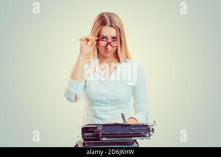Skeptical woman at typewriter looking at you camera doubtfully isolated on light green yellow background with copy space. Writer having doubts. Skepti