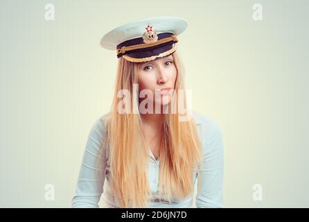 Skeptical woman looking at you camera doubtful with russian captain hat on head. Caucasian Business person in white formal shirt, long blonde hair iso Stock Photo