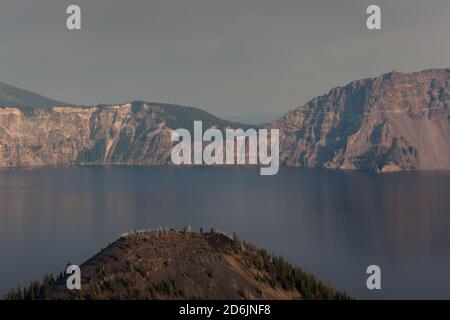 Looking over Wizard Island cone to Crater Lake and it's northeastern rim with smoke filled air from a nearby wildfire glowing in the afternoon sunshin Stock Photo