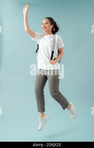 Full length photo of cheerful girl hold backpack jump run go lesson greet teacher classmates over blue background Stock Photo