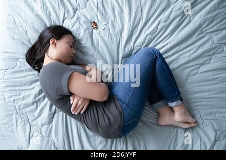 Top view of depressed woman lying on bed with pills Stock Photo