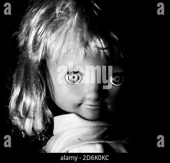 Creepy girl doll face. It seems like character of horror movie. Angry baby doll, fear of living ghost. Halloween concept. Black and white shot, low-ke Stock Photo