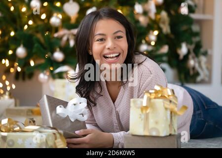 Smiling biracial woman lying under Christmas tree with gifts Stock Photo