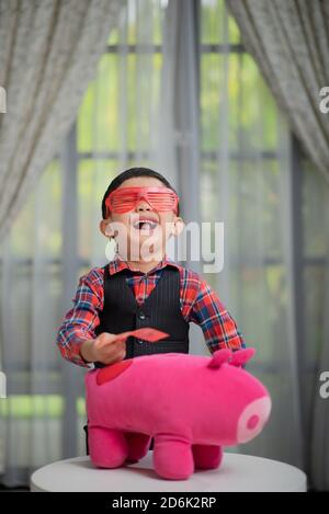 Asian Chinese boy, managing finances, putting money into piggy bank Stock Photo