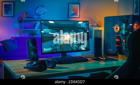 Powerful Personal Computer Gamer Rig with First-Person Shooter Game on Screen. Monitor Stands on the Table at Home. Cozy Room with Modern Design is Stock Photo
