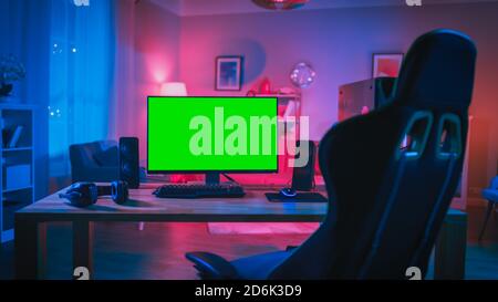 Powerful Personal Computer Gamer Rig with Mock Up Green Screen Monitor Stands on the Table at Home. Cozy Room with Modern Design is Lit with Pink Neon Stock Photo