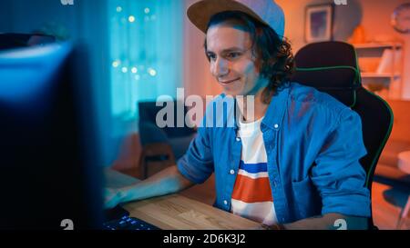 Excited Gamer in Cap Playing Online Video Game on His Personal Computer. Room and PC have Colorful Warm Neon Led Lights. Young Man has is Wearing a Stock Photo