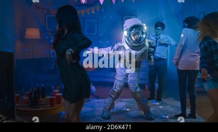At the College House Costume Party: Fun Guy Wearing Space Suit Dances Off, Doing Robot Dance Modern Moves. With Him Beautiful Girls and Boys Dancing Stock Photo