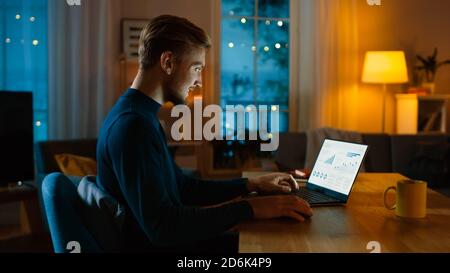 Evening at Home: Man Works on a Laptop Showing Statistical Infographic. Cozy Living Room with Warm Lights. Stock Photo