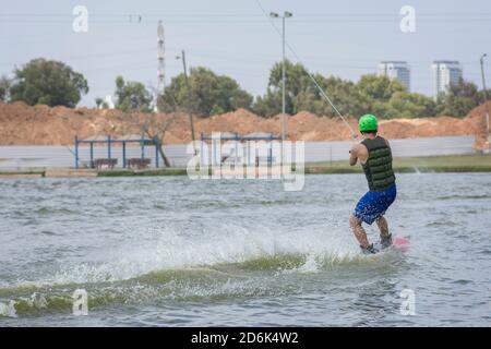 Man enjoying a Wakeboarding activity: a water sport in which the rider standing on a short board and pulled by a cables system in order to perform aer Stock Photo
