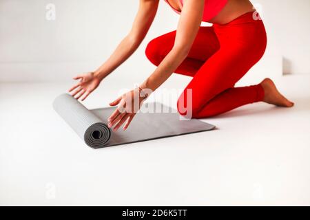 Side view of crop anonymous slim female in bright red top and leggings unrolling mat for yoga practice in white studio Stock Photo