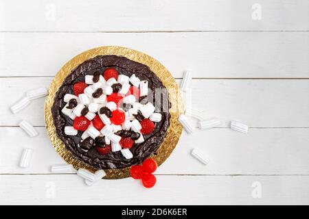 Homemade banana mousse cake decorated with ganache, marshmallows and berry-shaped marmalade on white wooden table. Top view. Copyspace. Stock Photo
