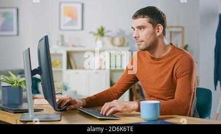 Portrait of Handsome Young Man Working on a Personal Computer from Home. In Cozy Bright Living Room Man Browses Through Internet. Stock Photo
