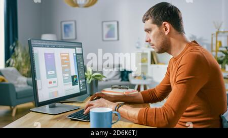 Handsome Software Engineer Works on a UX / UI Mobile App Template, Uses Personal Computer. Freelance Programmer Working At Home from Cozy Living Room. Stock Photo