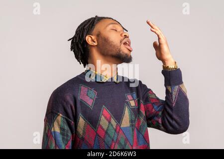 Depressed bored african man with dreadlocks yawning, tired after hard work day, need to rest, lack of sleep. Indoor studio shot isolated on gray backg Stock Photo