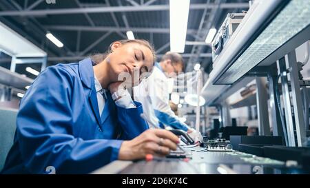Shot of a Tired Sleeping Female in Blue Work Coat at Her Working Place in Electronics Factory. High Tech Factory Facility with more Employees in the Stock Photo