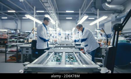 Shot of an Electronics Factory Workers Assembling Circuit Boards by Hand While it Stands on the Assembly Line. High Tech Factory Facility. Stock Photo