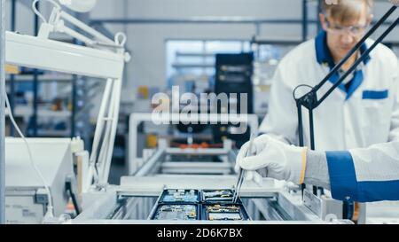 Shot of an Electronics Factory Workers Assembling Circuit Boards by Hand While it Stands on the Assembly Line. High Tech Factory Facility. Stock Photo