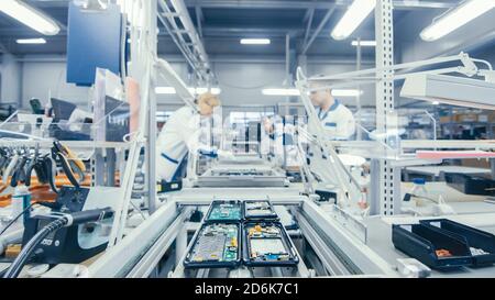 Shot of an Electronics Factory Workers Assembling Circuit Boards by Hand While it Stands on the Assembly Line. High Tech Factory Facility. Stock Photo