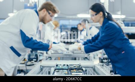 Shot of an Electronics Factory Workers Assembling Circuit Boards by Hand While it Stands on the Assembly Line. High Tech Factory Facility. Stock Photo