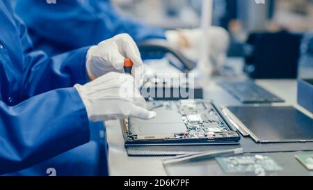 Close-Up of a Female Electronics Factory Worker in Blue Work Coat Assembling Laptop's Motherboard with a Screwdriver. High Tech Factory Facility with Stock Photo