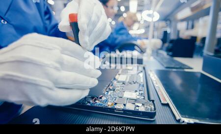 Close-Up of a Female Electronics Factory Worker in Blue Work Coat Assembling Laptop's Motherboard with a Screwdriver. High Tech Factory Facility with Stock Photo