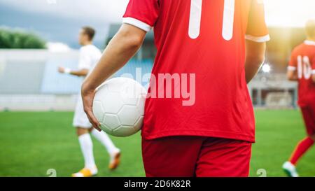 Shot of a Soccer Player Carrying Ball while Walking through the Field. In the Background Professional Team Training. Stock Photo