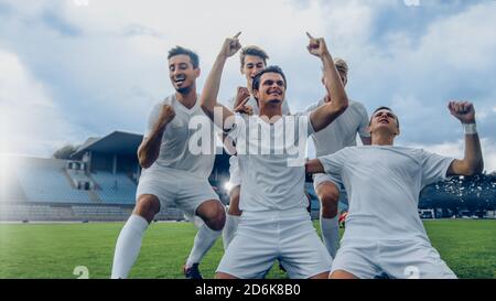 Captain of the Soccer Team Stands on His Knees Celebrates Awesome Victory, Makes YES Gesture Champion Team Joins Him. Successful Happy Football Stock Photo