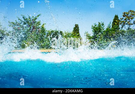 Many splashes in the swimming pool after jump diving over garden on sunny day Stock Photo