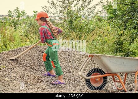 Outdoor activity. girl who is transporting rubble in a wheelbarrow. construction work. girl builder takes a shovel of rubble. hardworking youth. game of builder and construction. Stock Photo