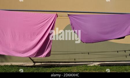 Pink and violet bed sheets hanging on a drying rack in the garden (Pesaro, Italy, Europe) Stock Photo