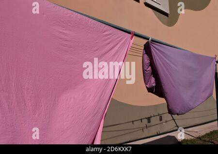 Pink and violet bed sheets hanging on a drying rack in the garden (Pesaro, Italy, Europe) Stock Photo