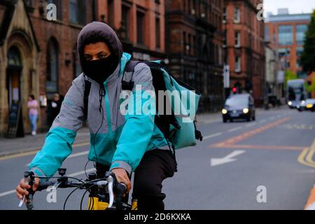 Manchester / United Kingdom - October 17, 2020: Delivery man with black face covering riding his bicycle in the Manchester street. Stock Photo