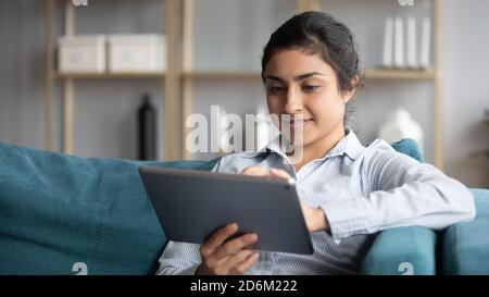 Indian woman resting on couch holding tablet enjoy online shopping Stock Photo