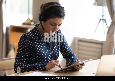 Indian businesswoman sitting at desk wear headset working on tablet Stock Photo
