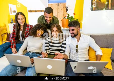 Mixed race happy friends group using three laptops at home on the sofa - Young people having fun together with social network looking at the computer Stock Photo