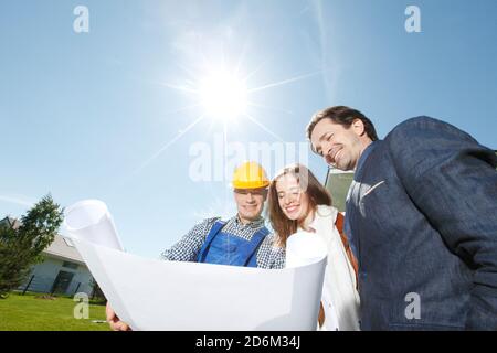 Foreman showing holding house design construction plan to a happy young couple new house real estate concept Stock Photo