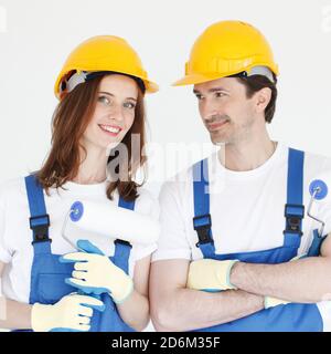 Two young workers in uniform of coverall and hardhat with paint rollers Stock Photo