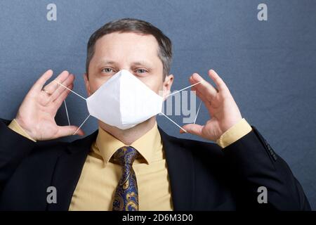 Portrait of a man in a suit with a tie. Sits at the table and puts on a medical mask. Stock Photo